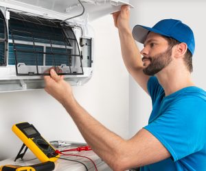 Installation service fix  repair maintenance of an air conditioner indoor unit, by cryogenist technican worker checking the air filter in blue shirt and baseball cap